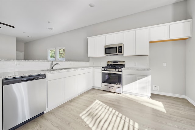 kitchen featuring white cabinets, light stone countertops, sink, stainless steel appliances, and light wood-type flooring