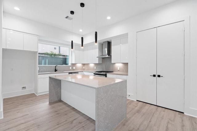 kitchen featuring wall chimney exhaust hood, hanging light fixtures, light hardwood / wood-style floors, and white cabinetry