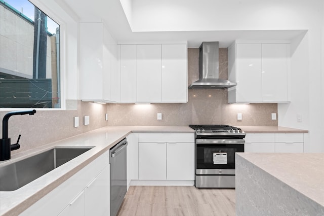 kitchen featuring stainless steel appliances, white cabinets, wall chimney exhaust hood, sink, and light hardwood / wood-style floors