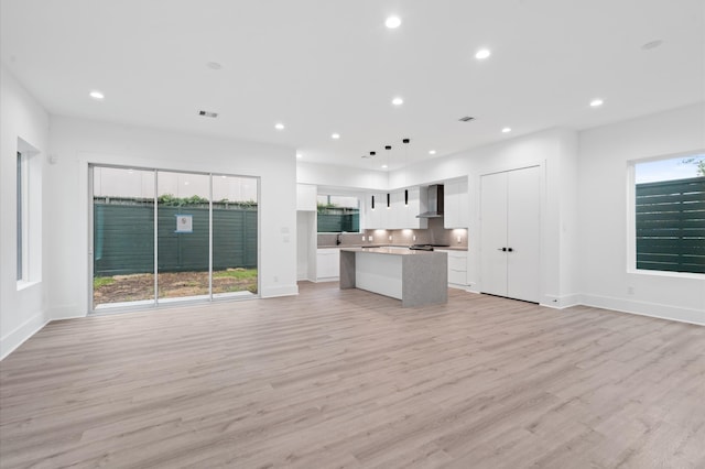 kitchen featuring sink, a kitchen island, wall chimney range hood, white cabinetry, and light hardwood / wood-style floors