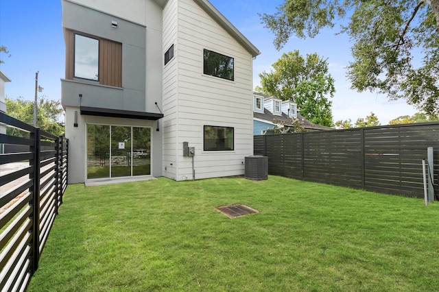 rear view of house with central AC unit and a yard