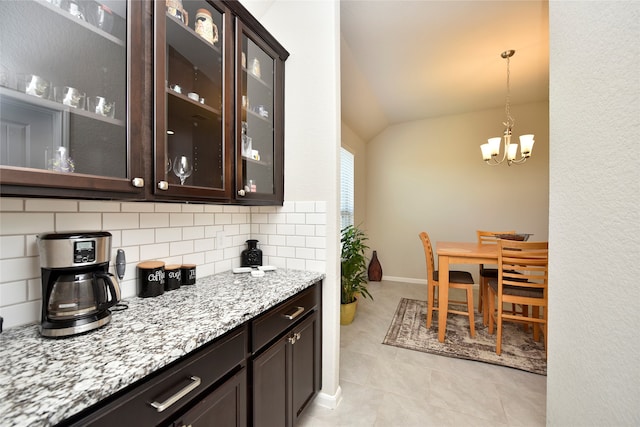 kitchen featuring dark brown cabinetry, light tile patterned flooring, lofted ceiling, tasteful backsplash, and light stone countertops