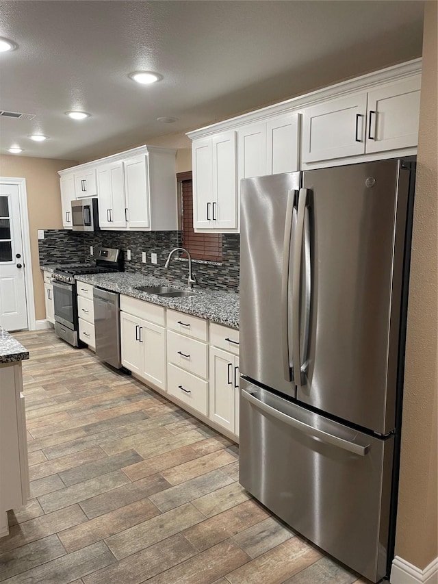 kitchen with light stone counters, stainless steel appliances, white cabinetry, and sink