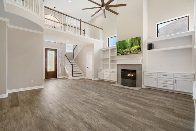 unfurnished living room with dark hardwood / wood-style flooring, a tile fireplace, crown molding, a high ceiling, and ceiling fan