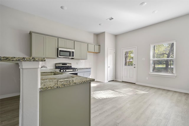 kitchen featuring light stone counters, visible vents, gray cabinets, stainless steel appliances, and tasteful backsplash