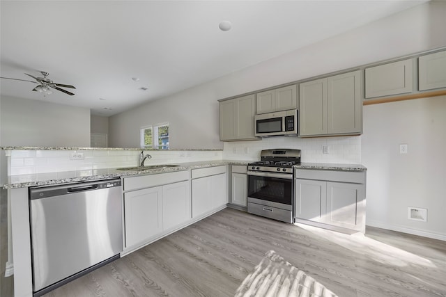 kitchen with light wood finished floors, tasteful backsplash, light stone counters, stainless steel appliances, and a sink