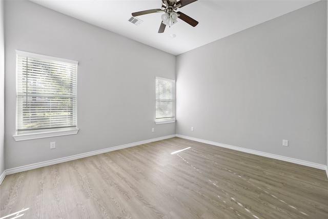 empty room featuring ceiling fan, visible vents, baseboards, and wood finished floors