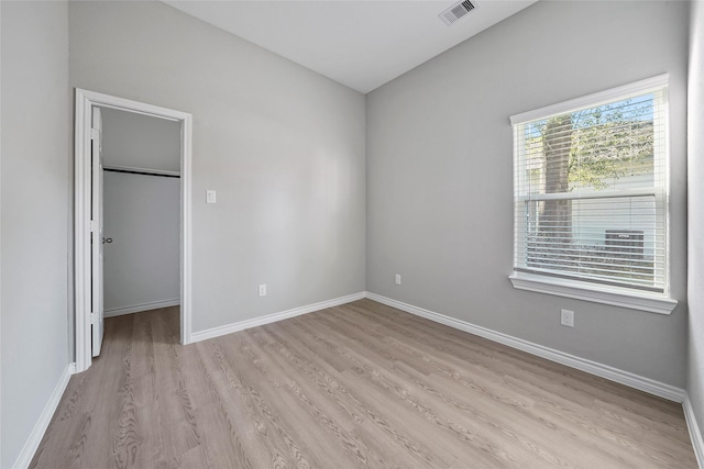 unfurnished bedroom featuring visible vents, baseboards, a spacious closet, and light wood finished floors