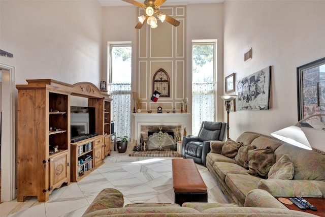 living room with ceiling fan, a towering ceiling, a fireplace, and a wealth of natural light