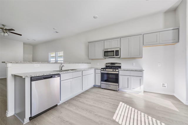 kitchen with appliances with stainless steel finishes, sink, kitchen peninsula, and light hardwood / wood-style flooring