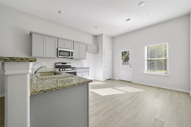 kitchen featuring gray cabinets, sink, stone counters, light hardwood / wood-style flooring, and appliances with stainless steel finishes