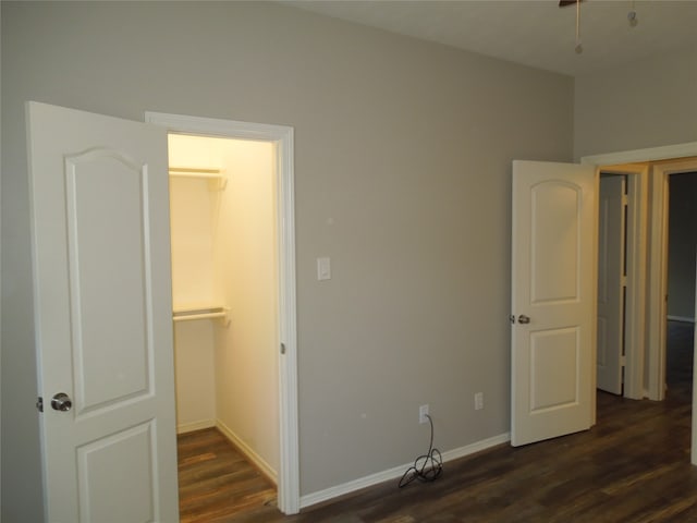 unfurnished bedroom with a spacious closet, a closet, and dark wood-type flooring