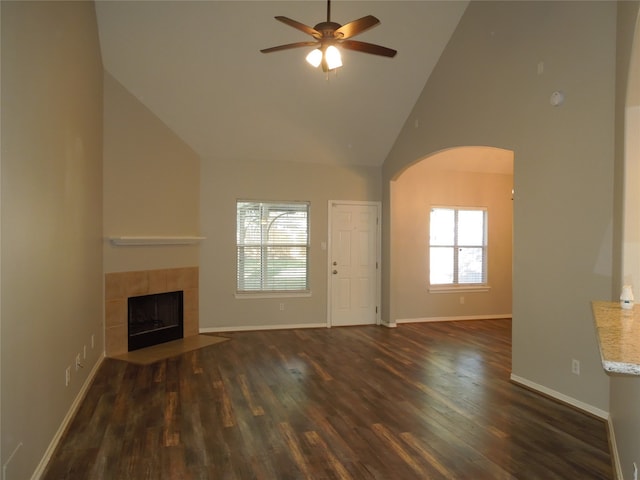 unfurnished living room with high vaulted ceiling, a tiled fireplace, ceiling fan, and dark wood-type flooring