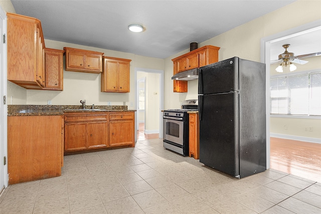 kitchen featuring ceiling fan, gas stove, dark stone counters, sink, and black fridge