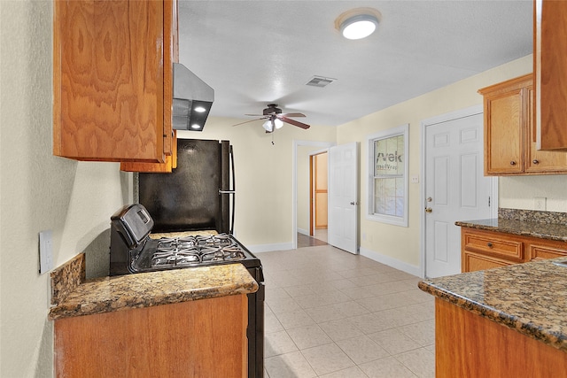 kitchen with exhaust hood, fridge, black range with gas cooktop, ceiling fan, and dark stone counters