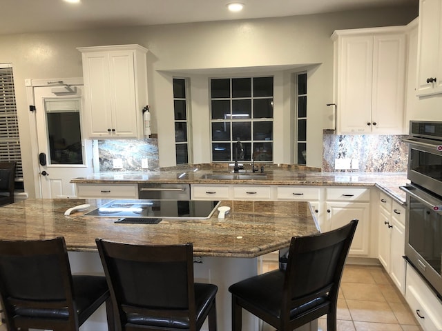 kitchen with sink, a kitchen breakfast bar, white cabinets, dark stone countertops, and light tile patterned floors