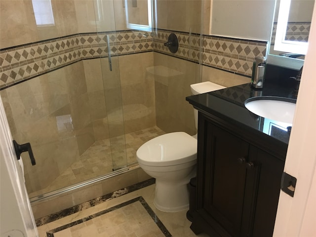 bathroom with tile walls, toilet, vanity, an enclosed shower, and tile patterned flooring