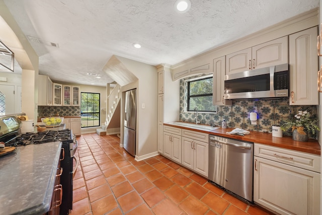 kitchen with backsplash, sink, stainless steel appliances, and wooden counters