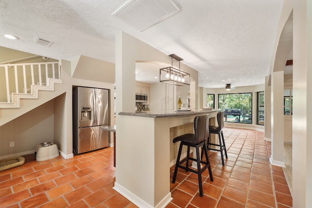 kitchen with a textured ceiling, stainless steel appliances, hanging light fixtures, and kitchen peninsula