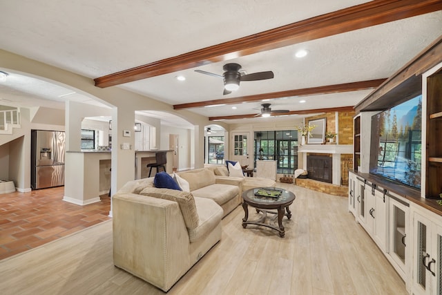 living room with light wood-type flooring, a textured ceiling, beamed ceiling, and ceiling fan