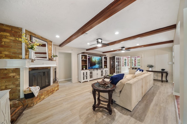 living room with light wood-type flooring, ceiling fan, beamed ceiling, and a brick fireplace