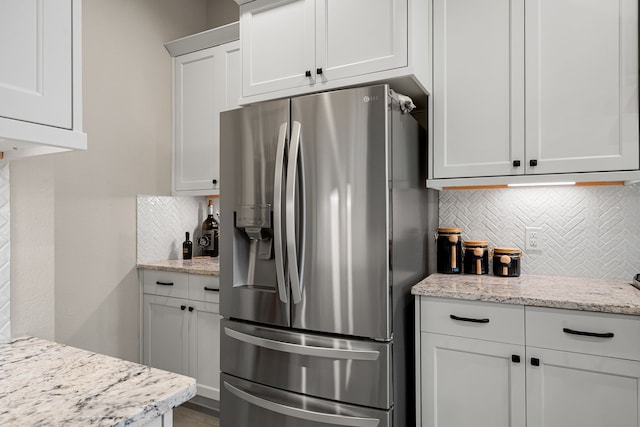 kitchen featuring light stone countertops, white cabinets, tasteful backsplash, and stainless steel fridge