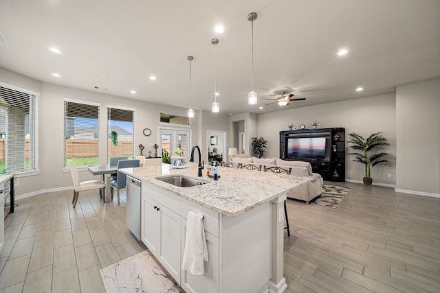 kitchen featuring white cabinets, light stone countertops, pendant lighting, a kitchen island with sink, and sink