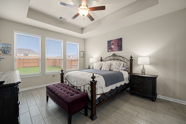 bedroom with multiple windows, light hardwood / wood-style floors, a tray ceiling, and ceiling fan