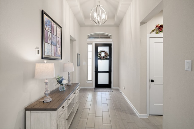 foyer entrance featuring a notable chandelier, a raised ceiling, and light wood-type flooring