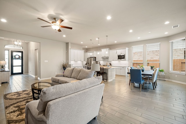 living room featuring ceiling fan with notable chandelier and light hardwood / wood-style floors