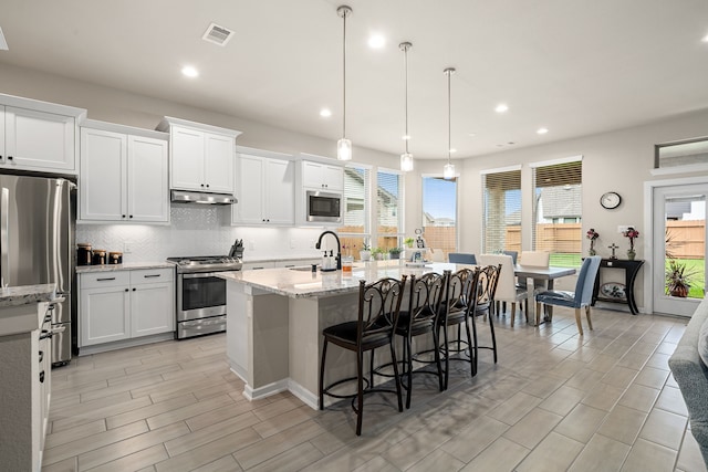 kitchen with stainless steel appliances, white cabinets, hanging light fixtures, and a kitchen island with sink