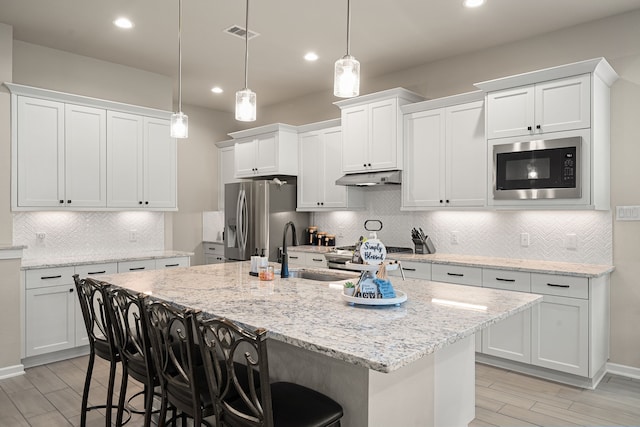 kitchen featuring white cabinets, a breakfast bar area, stainless steel appliances, and pendant lighting