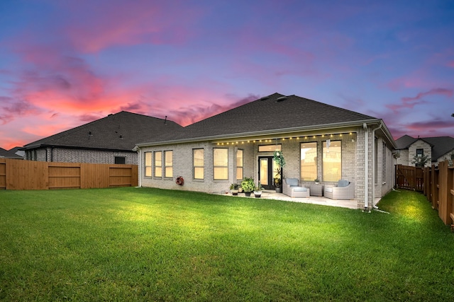 back house at dusk featuring a lawn and a patio