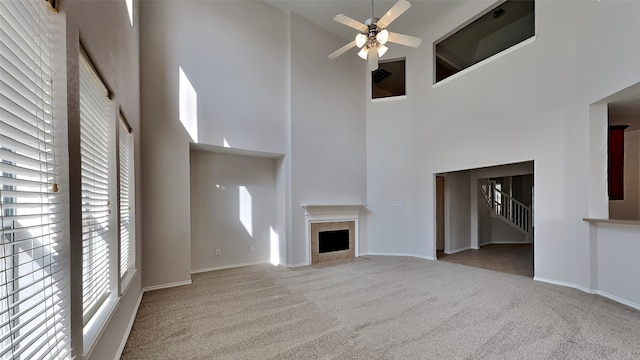 unfurnished living room featuring ceiling fan, light colored carpet, a towering ceiling, and a tile fireplace