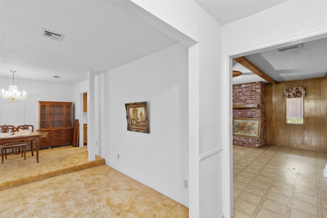 hallway with an inviting chandelier, wood walls, a textured ceiling, and light colored carpet