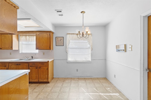 kitchen with a textured ceiling, hanging light fixtures, an inviting chandelier, and sink