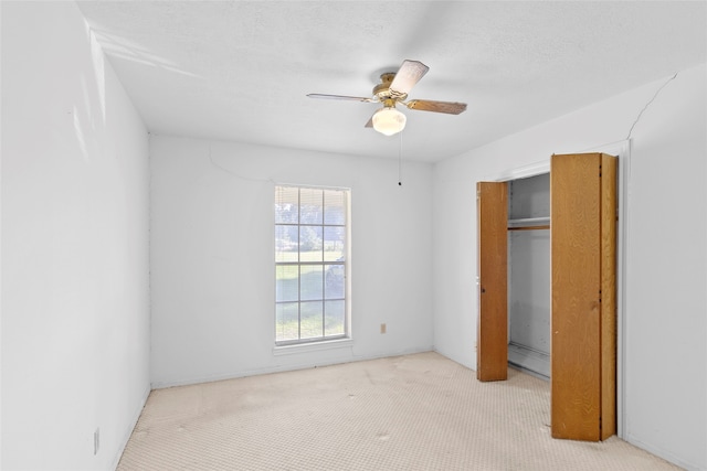 unfurnished bedroom featuring ceiling fan, a textured ceiling, a baseboard heating unit, a closet, and light carpet