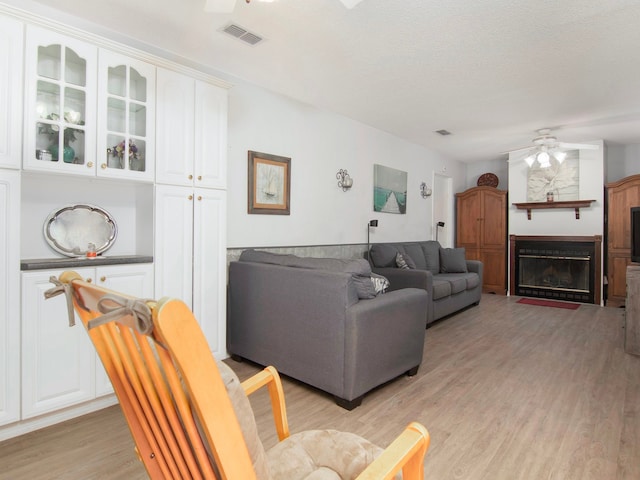 living room with ceiling fan, a textured ceiling, and light hardwood / wood-style flooring