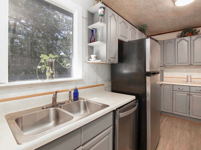 kitchen with appliances with stainless steel finishes, gray cabinetry, light wood-type flooring, and sink