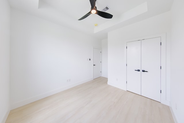 unfurnished bedroom featuring a raised ceiling, ceiling fan, a closet, and light hardwood / wood-style flooring