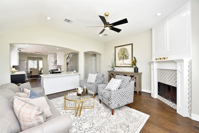 living room featuring ceiling fan, lofted ceiling, a tiled fireplace, and dark hardwood / wood-style flooring