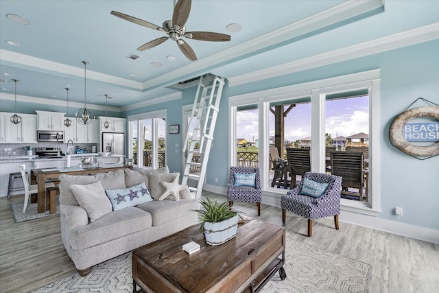 living room featuring ceiling fan, a tray ceiling, light wood-type flooring, and a healthy amount of sunlight