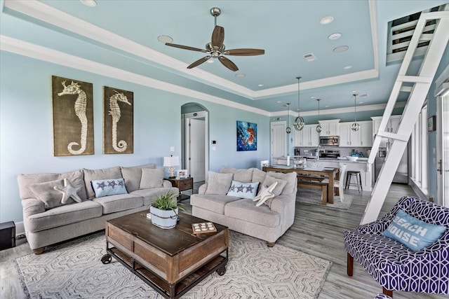 living room with light wood-type flooring, ceiling fan, a raised ceiling, and crown molding