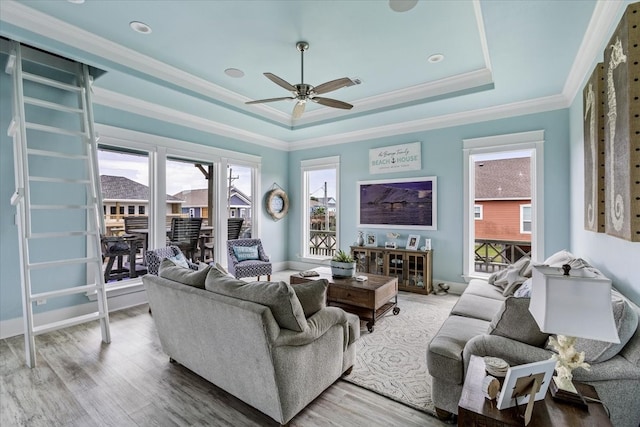 living room with wood-type flooring, crown molding, ceiling fan, and a raised ceiling