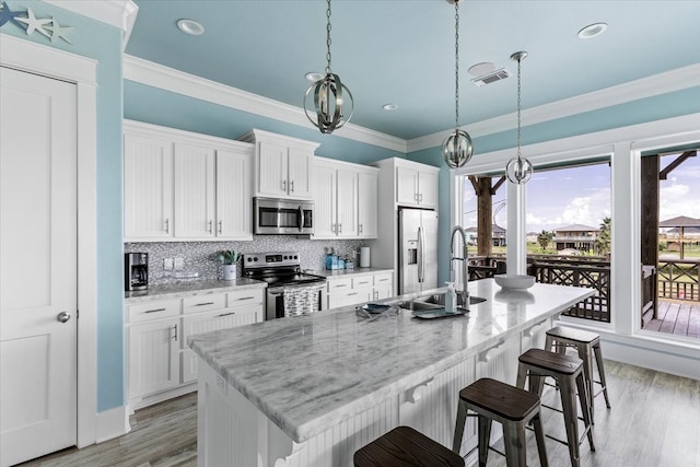 kitchen featuring appliances with stainless steel finishes, light hardwood / wood-style floors, white cabinetry, decorative light fixtures, and a center island with sink