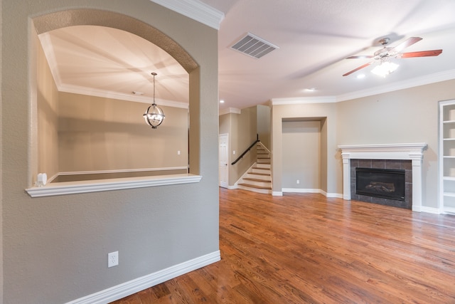 unfurnished living room with ceiling fan, a tile fireplace, hardwood / wood-style floors, and crown molding