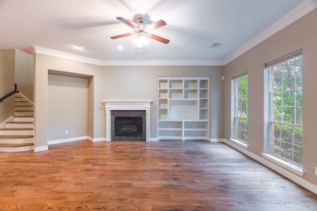 unfurnished living room featuring wood-type flooring, crown molding, a tiled fireplace, and ceiling fan