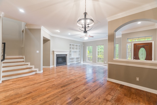 unfurnished living room featuring a tile fireplace, crown molding, ceiling fan with notable chandelier, and hardwood / wood-style floors