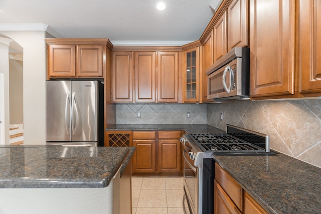 kitchen featuring light tile patterned floors, tasteful backsplash, appliances with stainless steel finishes, dark stone countertops, and crown molding