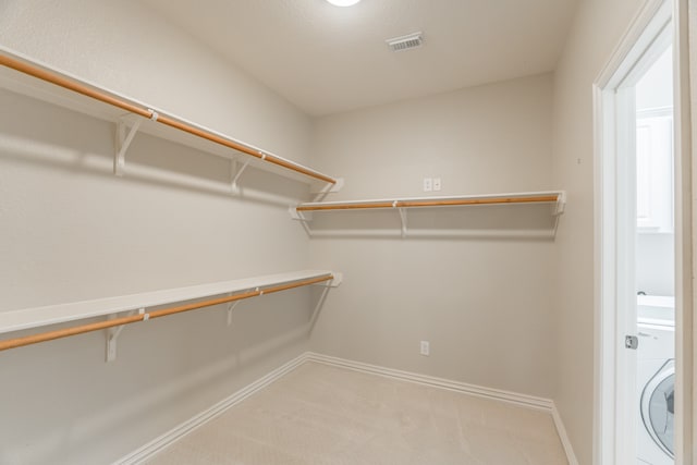 spacious closet featuring washer / clothes dryer and light colored carpet